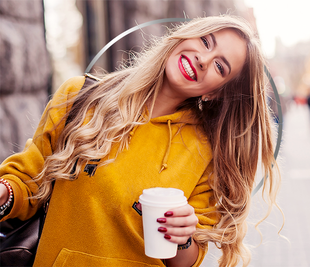Šťastná mladá žena v žltej mikine drží papierový pohár na kávu