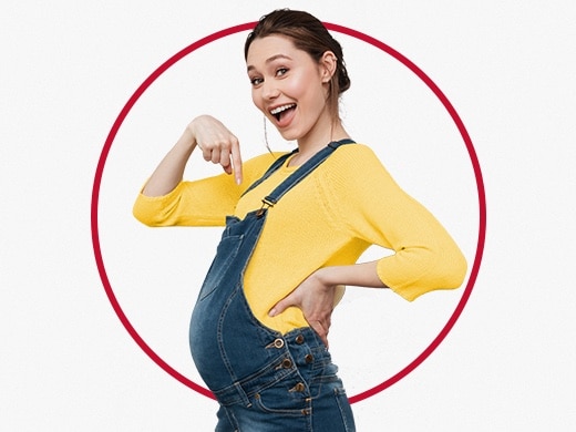 Mladá tehotná žena má na sebe žltý sveter a ukazuje na svoje tehotenské bruško